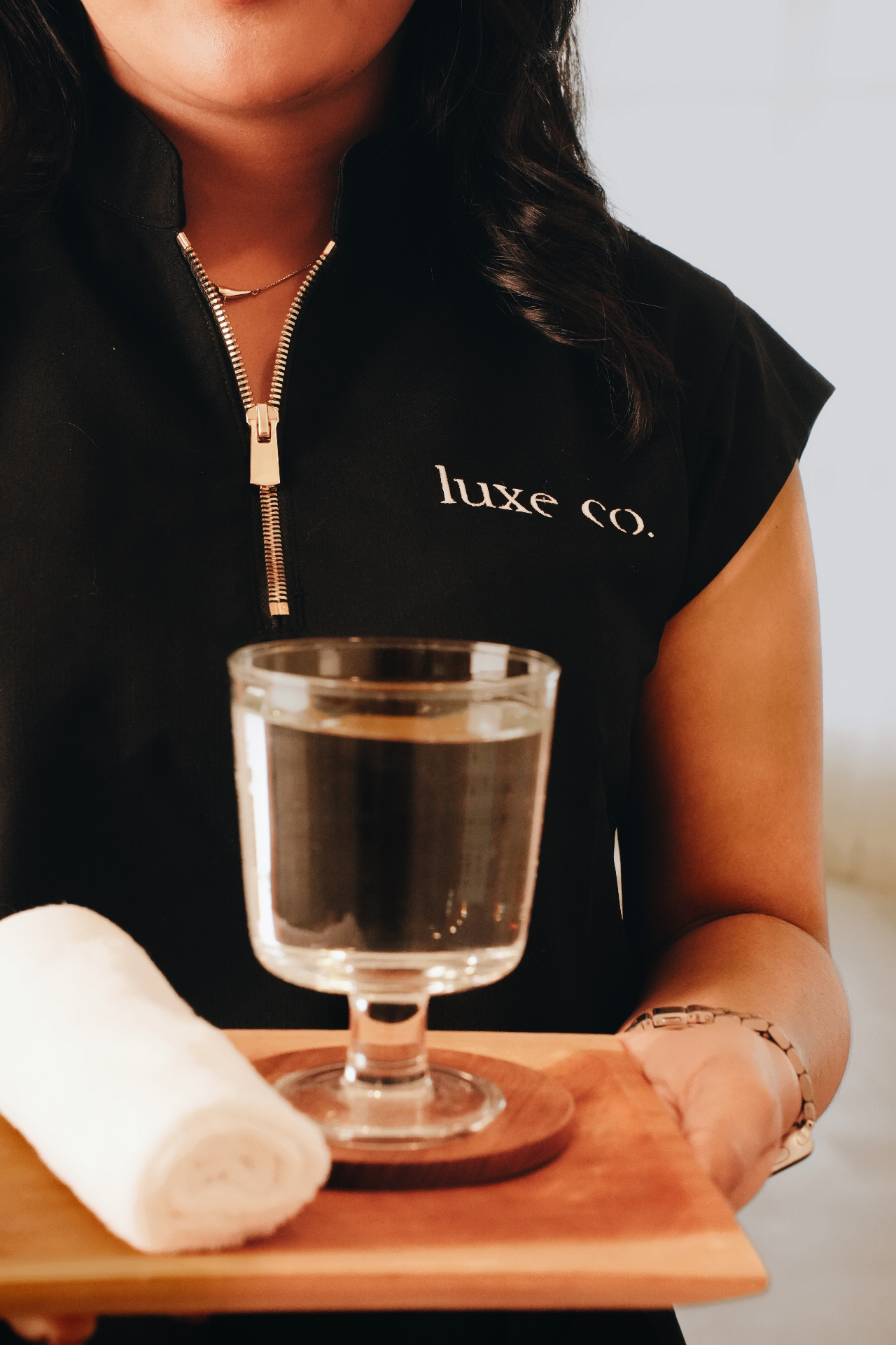 Luxe Co. therapist in branded uniform holding a service tray